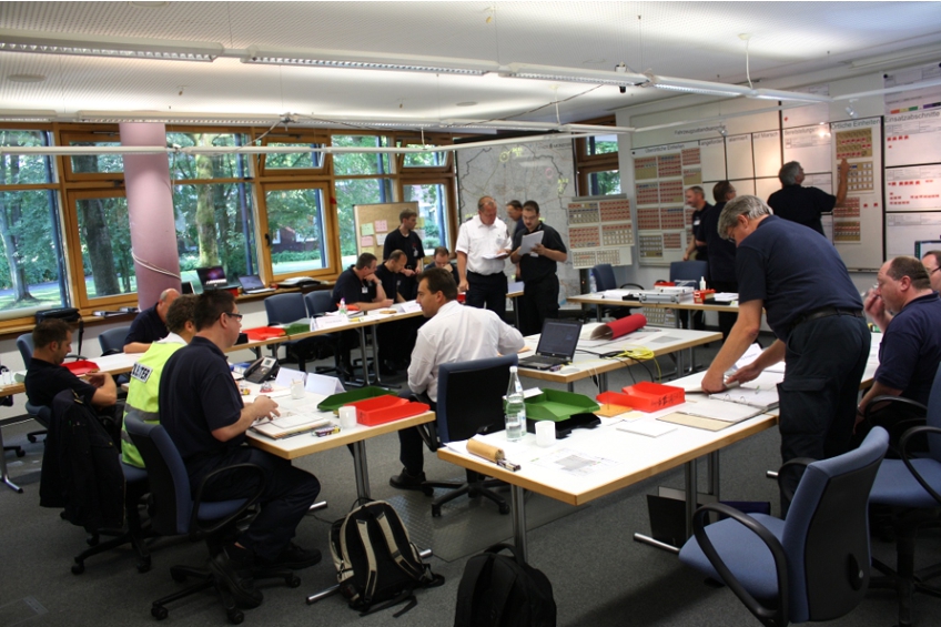 Staff exercise at State Fire Service Institute North Rhine-Westphalia. The case study’s goal is to recognize the interactions between staff members and objects – in this image: “conversation” (left/center), “analyzing a document together” (top center), and “editing a display” (top right).