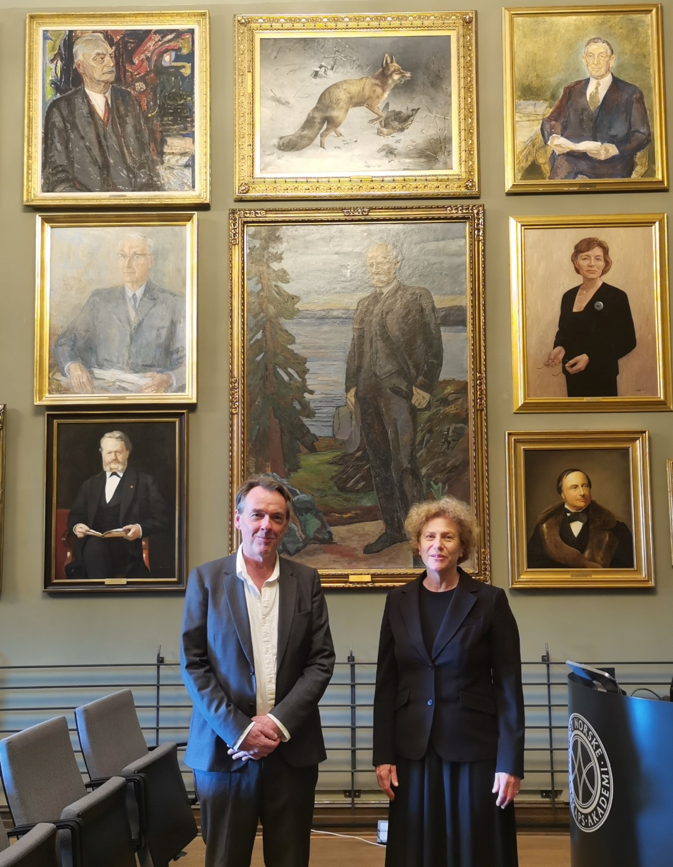 The 2022 Nansen Neuroscience Lecturers David Gems (left) and Henriette van Praag (right). The speakers are standing in front of the portrait of Fridtjof Nansen in the Kavli Lecture Hall, in the building of the Norwegian Academy of Science and Letters, Oslo, Norway. Photo by Evandro F. Fang.