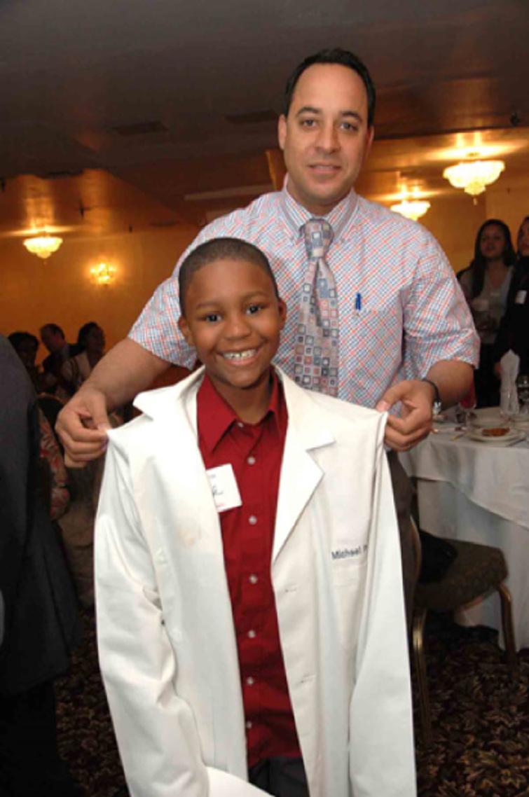At a Mentoring in Medicine event, a possible future healthcare professional gets the chance to model a lab coat with a MIM mentor.