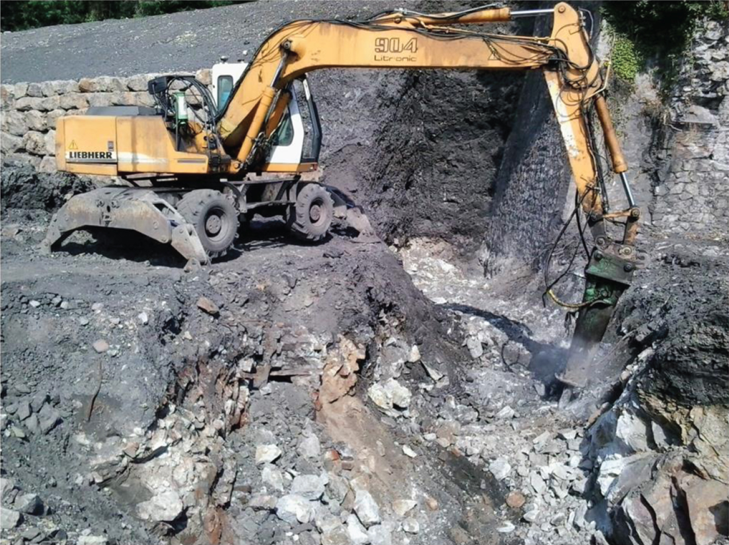 Wheel excavator operator working with a rock breaker for foundations preparation.
