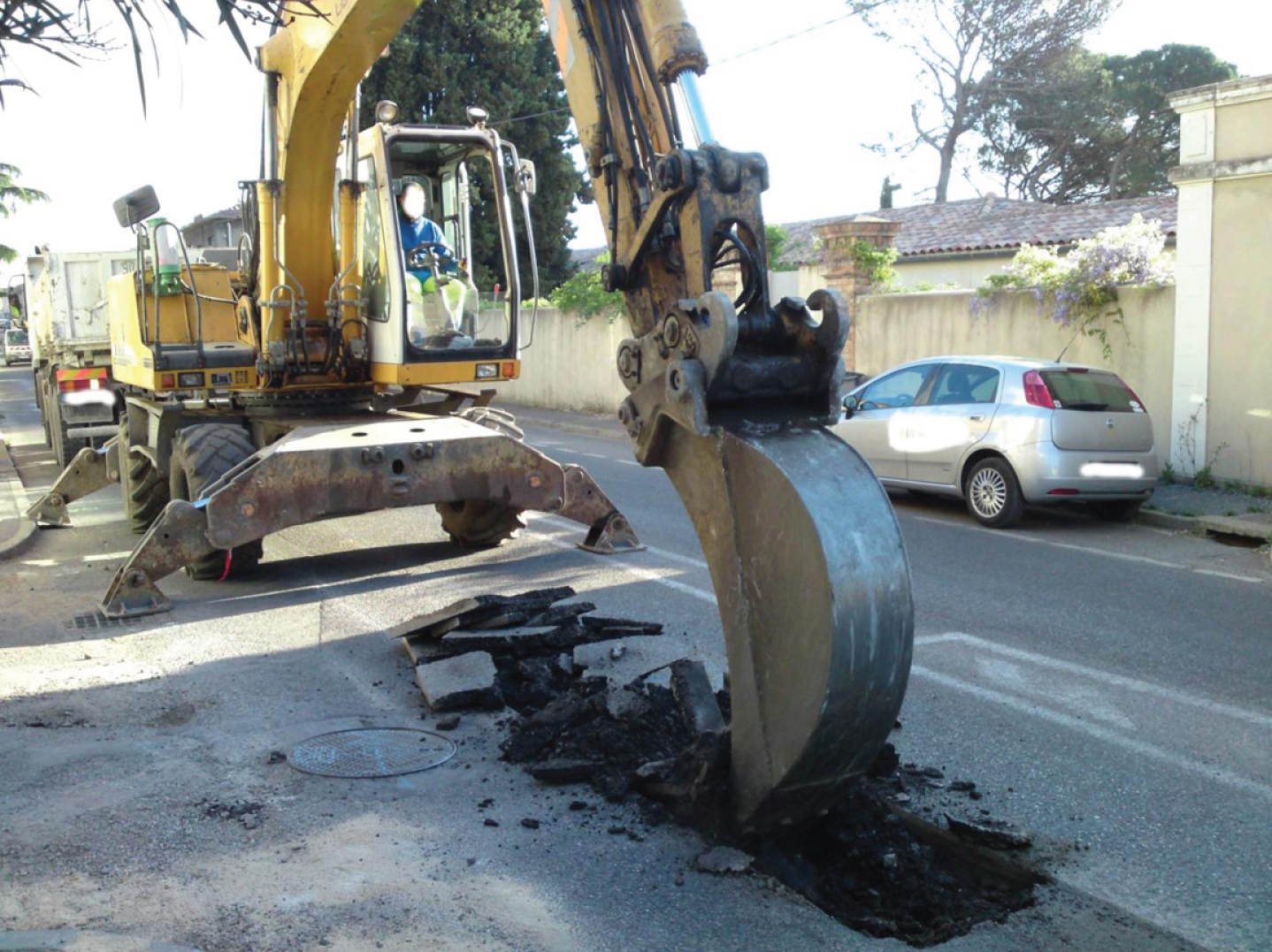 Worker driving a pneumatic shovel and digging a trench on a road.